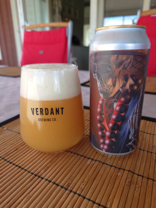 Ölglas med skum och en burk med konstverk av ett skelett, på ett bambuunderlägg.