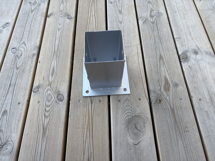 Metallisk stolpfot med fyrkantig öppning på en trädäckad altan, förberedd för montering av pergola.