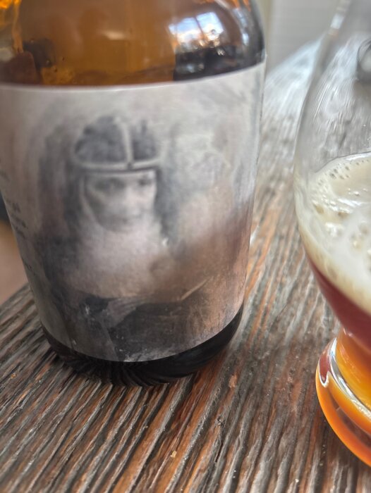 Flaska av belgisk strong ale från Vreta klosterbryggeri med suddig etikett, bredvid glas med öl på ett rustikt träbord.