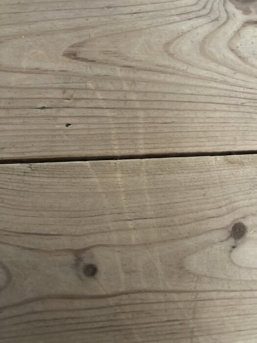 Repor i ett obehandlat trägolv, synliga parallellt med träets ådring. Golvet är skurat med såpa och reporna är djupa nog att kännas med handen.