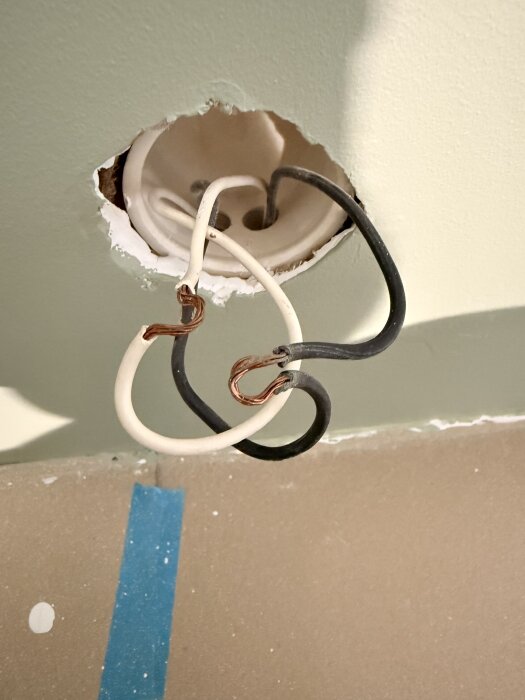 Elluttag med exponerade elledningar, svart och vit, som sticker ut från väggen. Används i diskussion om hur ledningarna ska kopplas.