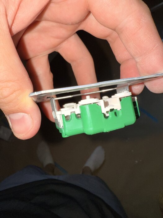 Hand håller på en eluttagsskontakt med gröna och vita komponenter, tagen under installation efter målning.