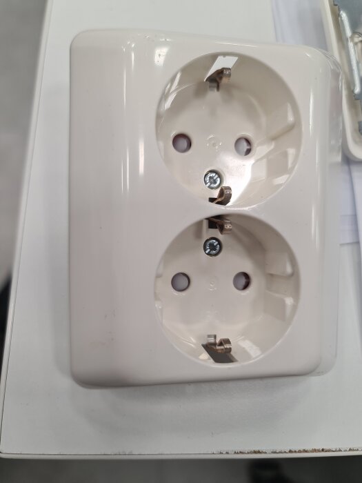 Dubbel vägguttag med jordningshål utan synliga kabelskruvar, fotograferad från ovan.