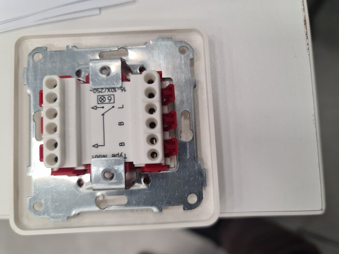 Elektrisk strömbrytare utan kabelskruvar med hål märkta A och B, monterad på metallplåt.