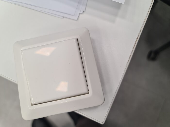 Vit ljusströmbrytare monterad på en vit vägg, delvis täckt av några papper ovanpå.