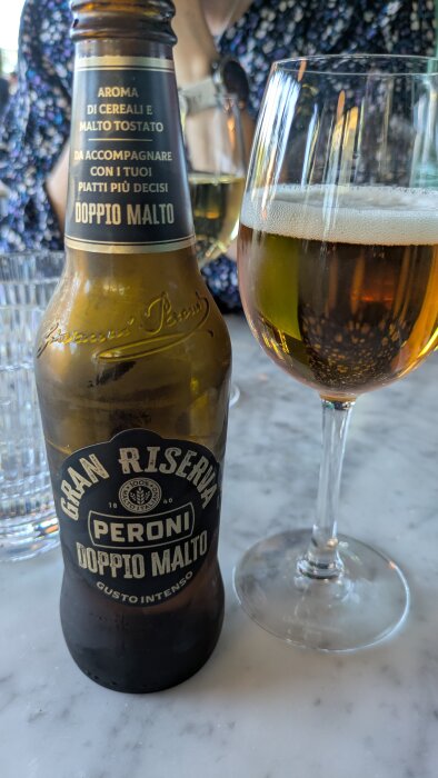 Flaska Peroni Doppio Malto och ett glas öl på ett marmorbord på en italiensk restaurang.
