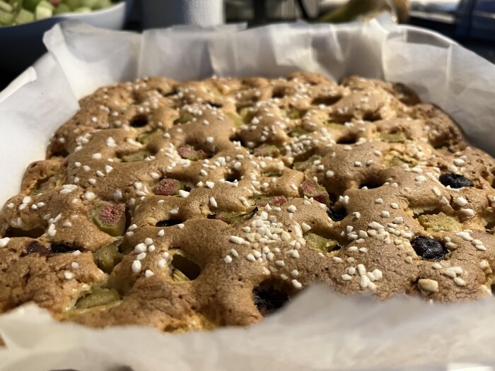 En rabarberkaka med blåbär och kokos syns i en bakform, innan den bakas i ugnen. Täckt med strösocker på toppen.