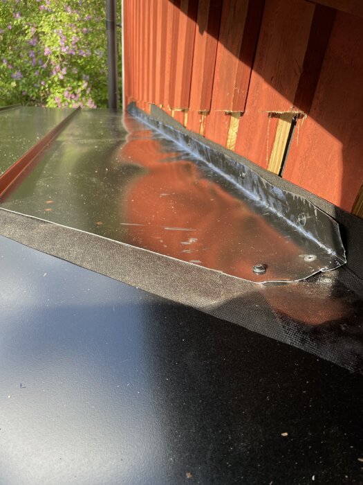 Bucklig falsad bandplåt mot röd vägg på ett valmat tak i ett gammalt torp, med synliga skruvar och inkilad kantlist.