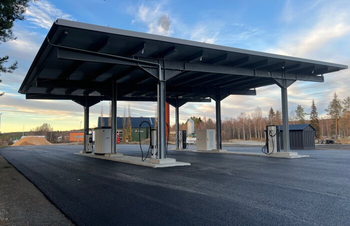 Laddplats med rymlig infart för stora fordon och släp under ett skyddande tak mot en lantlig bakgrund.