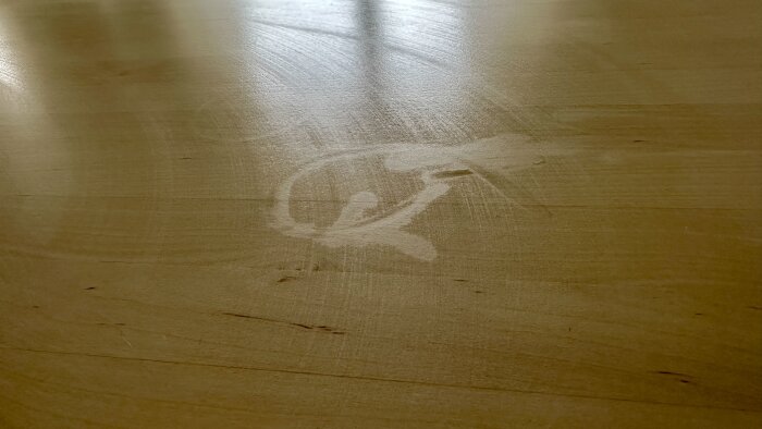 Vattenfläck på ett lackat träbord, orsakad av att ett glas placerats där.