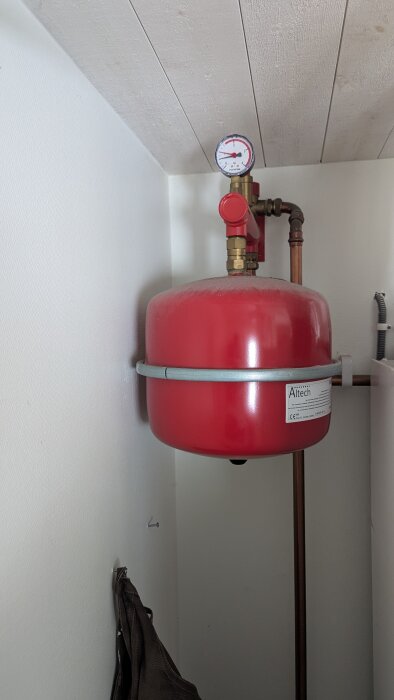 Röd expansionskärl från Altech, monterat på väggen med en tryckmätare ovanpå. Koppel av kopparrör är anslutet.