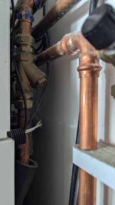 Installation av bergvärmepump med kopparrör och ventiler; en del är dammig.