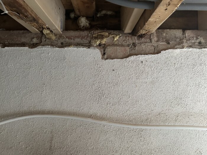 Källarvägg med grovputsad yta och synligt hålrum vid takbjälkarna, del av renoveringsprojekt av tvättstuga med behov av lagning och omputsning.