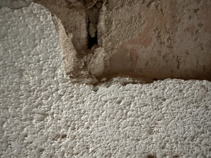 Närbild på putsad vägg med grov struktur och mindre skada i en källartvättstuga under renovering.