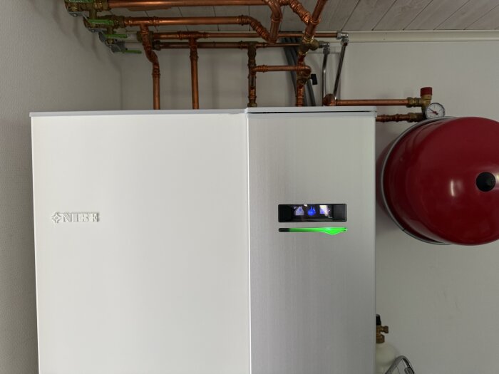 Bilden visar en NIBE bergvärmepump med kopparrör och expansionskärl monterade ovanför.