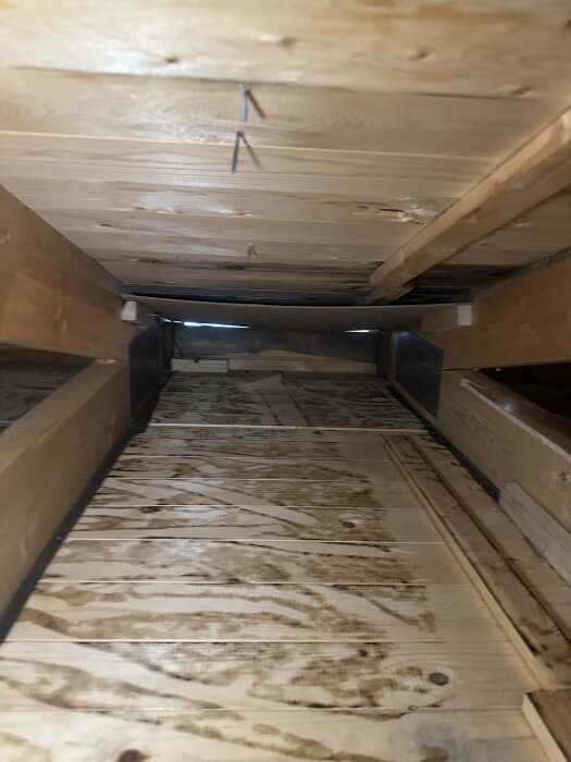 Ett vindutrymme med träråspont och synliga mörka fläckar från tidigare tjärpapp installation visas, med trästrukturer och några spikar.