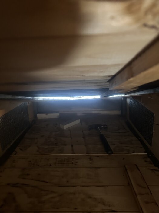 Vy av vind med råspontgolv, synliga mörka fläckar efter tjärpapp, samt liggande hammare i förgrunden inom ett isoleringsprojekt.