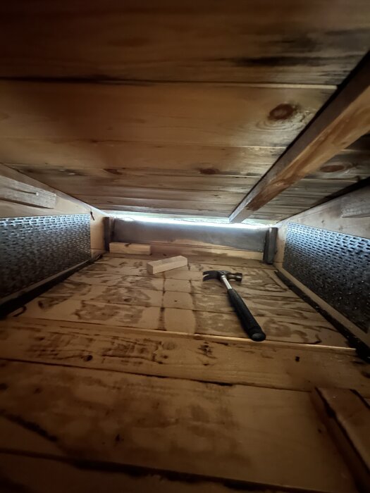 Vindsvåning med råspontgolv, träkloss och hammare, visar mörka fläckar efter tjärpapp under förberedelse för FTX-installation.