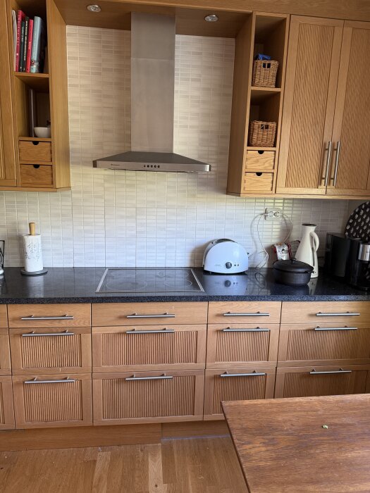 Ekfärgat Ikea-kök med ribbade luckor, svart bänkskiva och vitkaklad vägg. Vit brödrost och kaffebryggare syns på bänken.