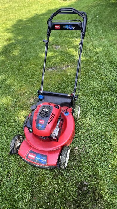 Röd Toro gräsklippare på gräsmatta, handtag högt upp och slapp koppling, bakhjul problematiska vid körning.
