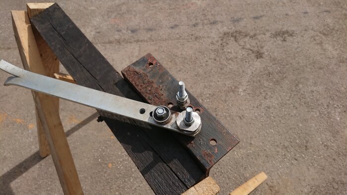 Hemmagjord bockningsjigg i metall med skruvar, placerad på en träram utomhus, användes vid garagebygge.