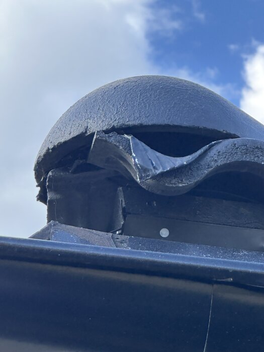 Defekt hörnkonstruktion på nylagt tak, med oregelbundet monterade takplattor synliga, mot en bakgrund av blå himmel och moln.