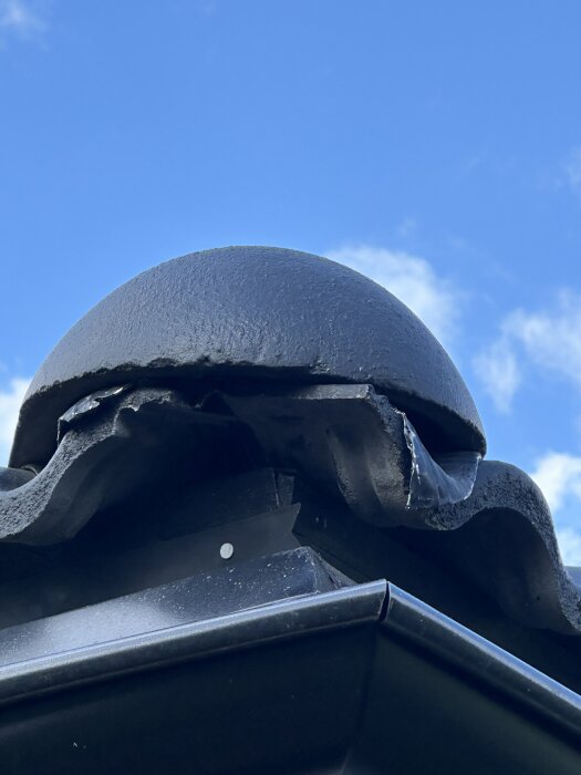 Takets hörn med synliga skador och ojämnheter i takpannorna mot blå himmel.