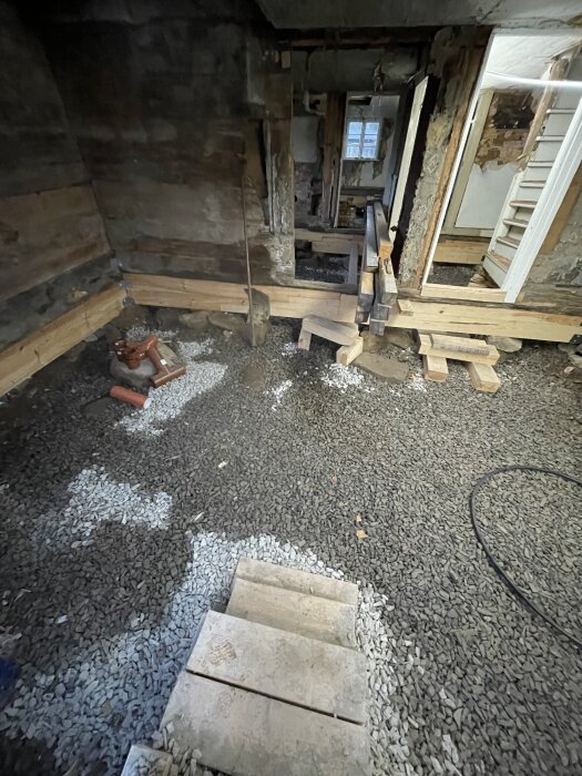 Renoveringsprojekt med exponerad grund, synlig makadam under trägolv. Mörka och ljusa stenområden som antyder fuktvariationer i januari.