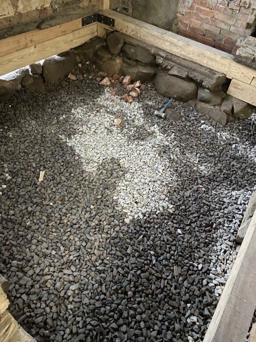 Grusbelagd yta i ett rum med trä- och stenväggar, ljusskiftningar från mörkt till ljust grus i januari.