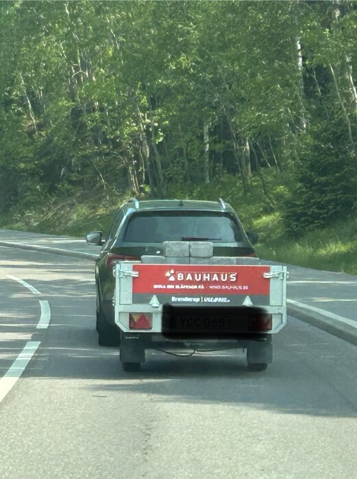Bil med släpvagn lastad med stenar från Bauhaus på landsväg.