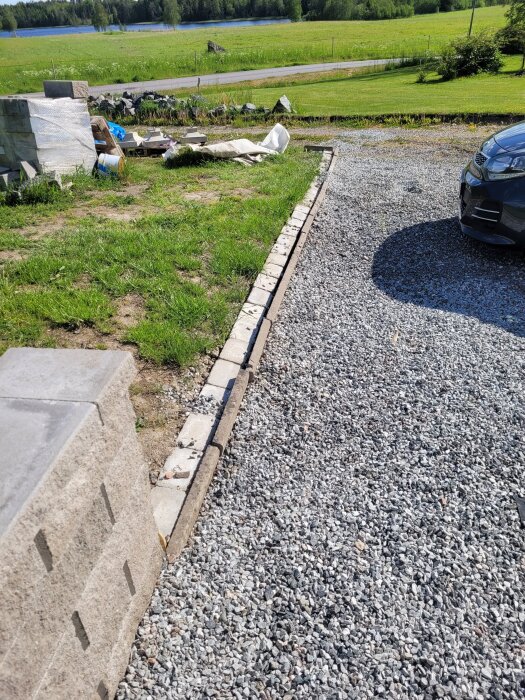 Stödmur med fyra block och geonät samt grusad yta, bredvid mindre mur utan makadam, i en trädgårdsmiljö.