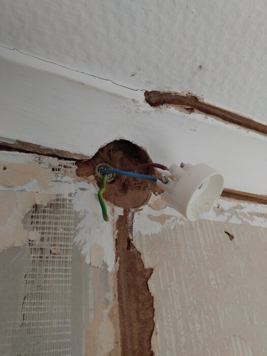 Öppen vägg med elektriska ledningar och ett elektriskt uttag som hänger löst, delvis exponerade i ett renoveringsprojekt.