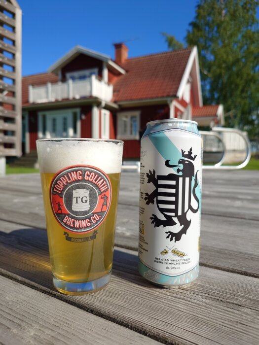 Ölglas och burk på träbord utomhus framför röd stuga med vita knutar.