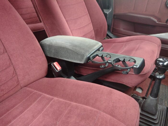 Bilinteriör med två vinröda säten, ett grått armstöd och en svart dryckeshållare i en Saab.