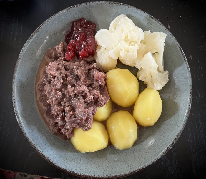 Kålmaja, kokt potatis, kokt blomkål och lingonsylt på en tallrik.