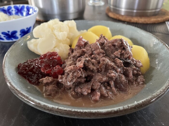 Tallrik med kålmaja, kokt potatis, kokt blomkål och lingonsylt.