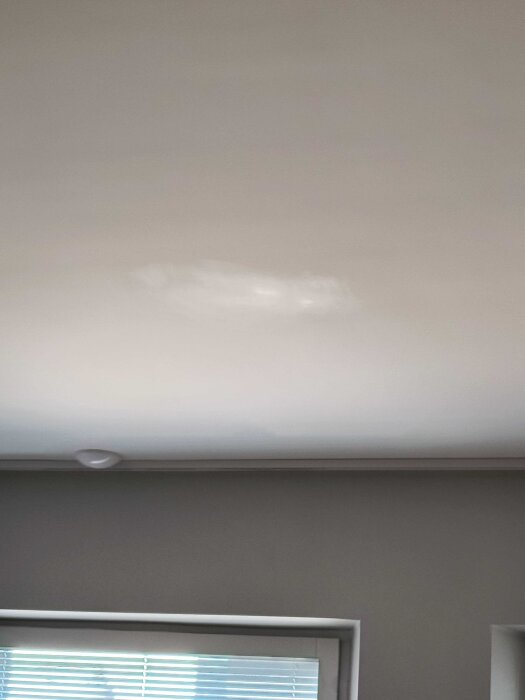 Skada på ett vitt innertak efter rengöringsförsök, med en ljus fläck synlig nära hörnet av bilden.