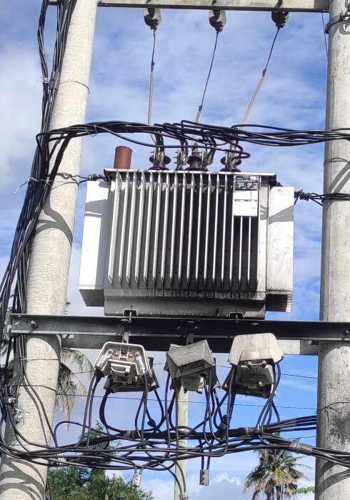 Transformator vid elstolpe utan skyddsbarriär, med flera kablar anslutna i soligt väder.