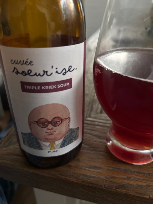 Flaska och glas med Cuvée Solur'ise Triple Kriek Sour öl, 8% alkohol, på ett träbord.