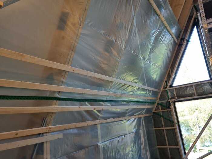 Byggprojekt i triangulär struktur med plast och träreglar på väggarna; stora fönster och en synlig ställning.