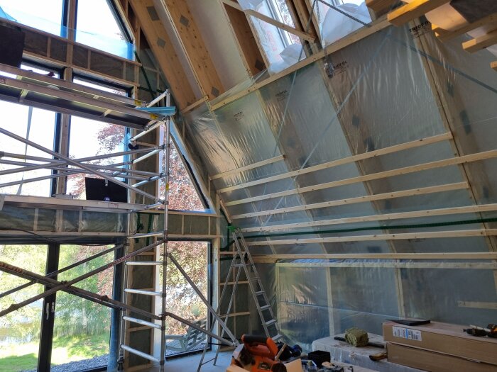 Byggarbetsplats med trästomme, plastfolie och byggnadsställning inomhus nära stora fönster.