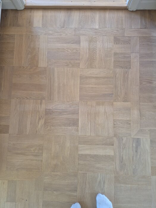 Nybehandlat stavparkettgolv med synliga ljusa partier där tejp tidigare suttit, visar behandlingsresultat och ytskillnader efter slipning och lackning.