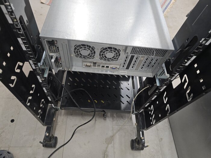 Server monterad i ett rack med utdragsskenor, synliga kablar och kylfläktar, i ett maskinrum under installation och kabeldragning.