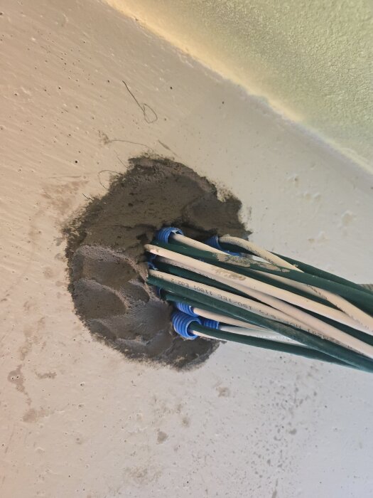 Nätverkskablar genom taket insmorda med betongspackel, med blå flexslangar och vitputsad yta.