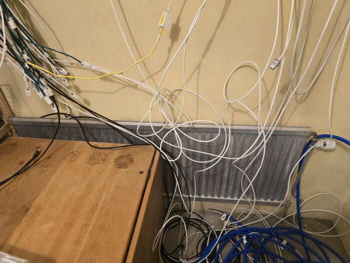 Kabelhärva och serverutrustning i ett hobbyrum, med flexslangar och nätverkskablar hängande ovanför ett gammalt element.