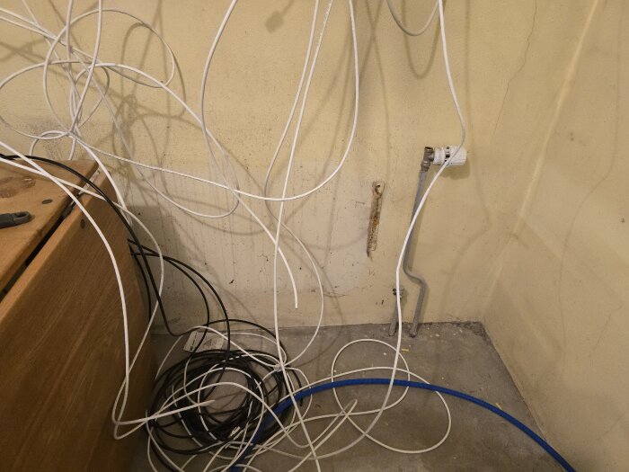 Bunt vita och svarta kablar hänger och ligger i hörn av rum med rör på väggen.