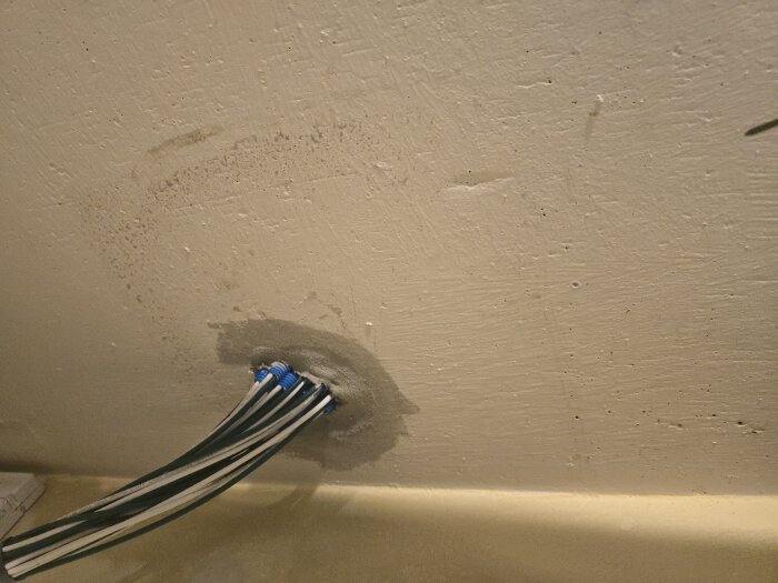 Elledningarna går in i en vit vägg genom ett runt hål, där flera kabeländar med blå kopplingar är synliga.