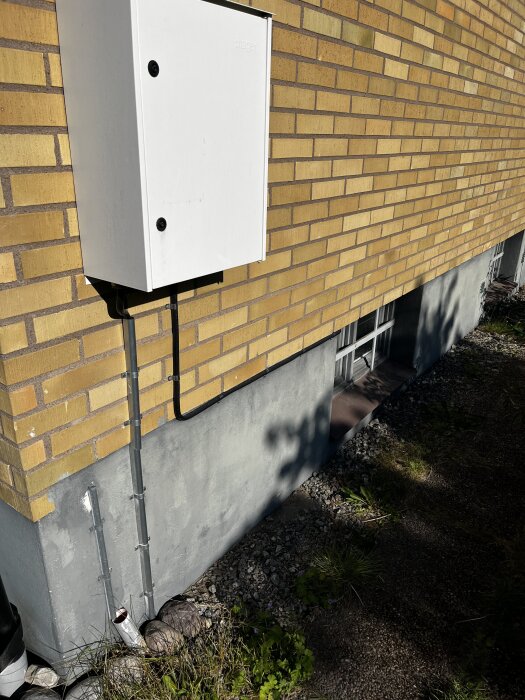 Kabelskydd på fasad, elledning går in i ett vitt skåp på gul tegelvägg cirka 1 meter från marken. Finns fråga om ytterligare skydd.
