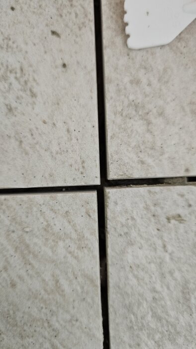 Närbild av fyra beige klinkerplattor med synlig skevning i fogarna, där plattorna inte linjerar exakt i sina hörn.