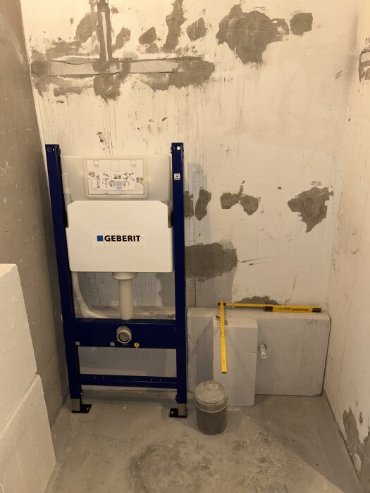 Vägghängt toalettfixtur från Geberit monterat i rå betongvägg med synliga rör och reglar. Måttstockar visar avstånd och placering.
